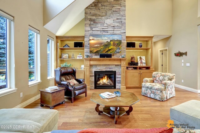 living area featuring a stone fireplace, a towering ceiling, baseboards, and light wood finished floors