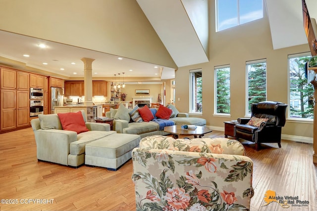 living room featuring baseboards, decorative columns, a fireplace, light wood-style floors, and a towering ceiling