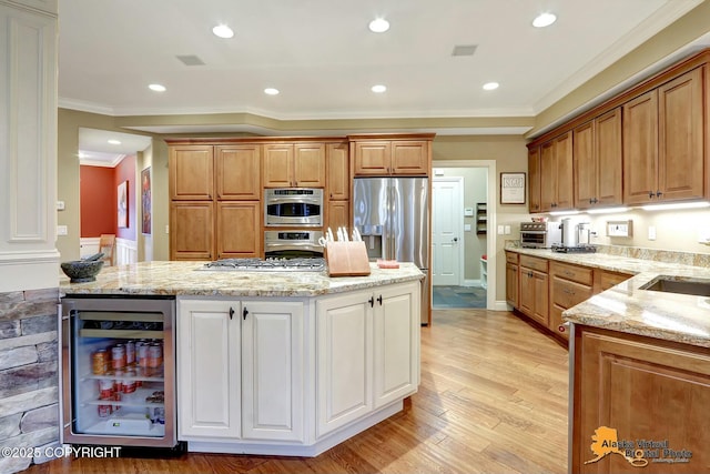 kitchen featuring beverage cooler, ornamental molding, light wood-style flooring, stainless steel appliances, and light stone countertops