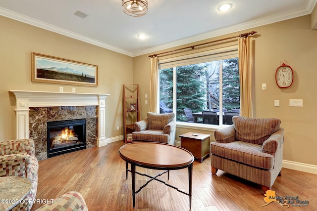 living room featuring wood finished floors, baseboards, a high end fireplace, and ornamental molding