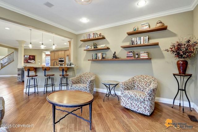 sitting room with visible vents, light wood-style flooring, crown molding, and ornate columns