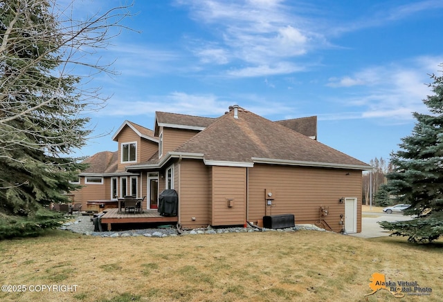 rear view of property with a wooden deck, a yard, and roof with shingles