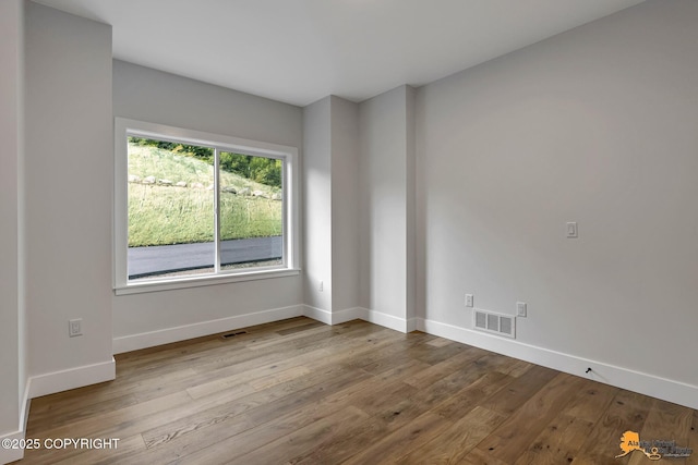 spare room with wood finished floors, visible vents, and baseboards