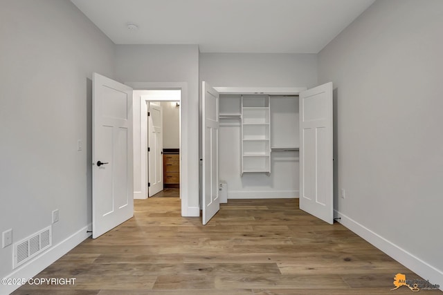 unfurnished bedroom with a closet, visible vents, baseboards, and wood finished floors