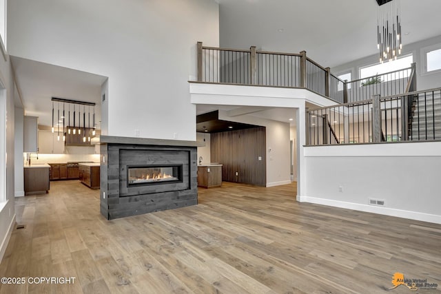 unfurnished living room featuring light wood-style flooring, stairway, baseboards, a high ceiling, and a multi sided fireplace