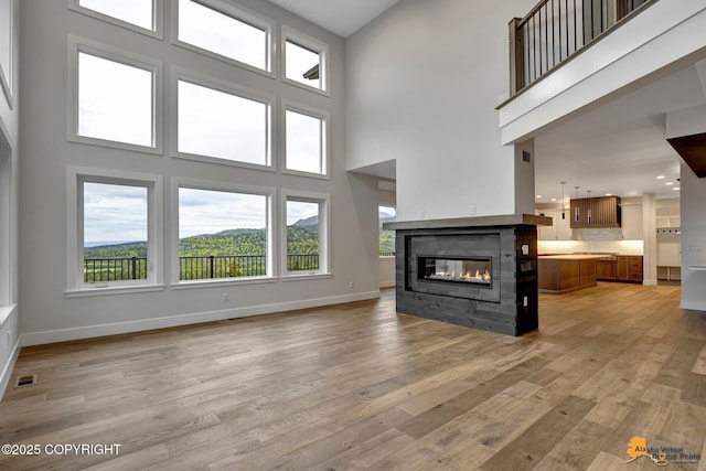 unfurnished living room featuring baseboards, a multi sided fireplace, visible vents, and light wood finished floors