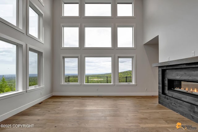 unfurnished living room with baseboards, a glass covered fireplace, a towering ceiling, and light wood finished floors