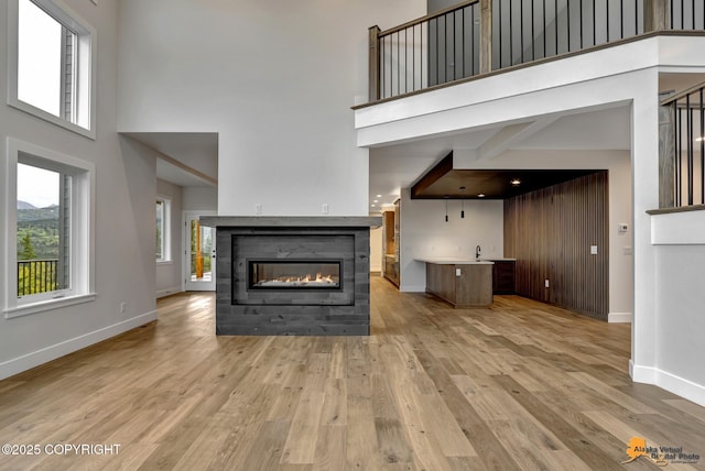 unfurnished living room featuring a glass covered fireplace, light wood-type flooring, and a towering ceiling