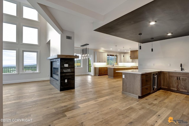 kitchen with visible vents, a multi sided fireplace, light countertops, light wood-style flooring, and a sink