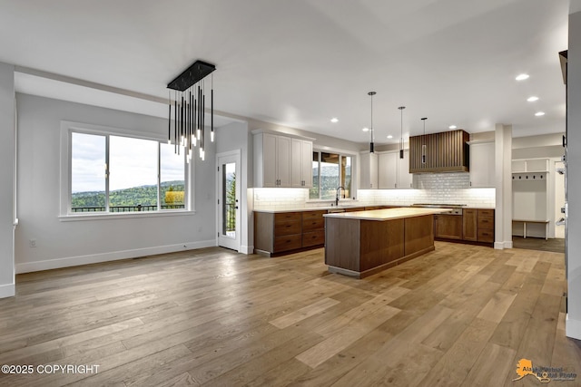 kitchen with tasteful backsplash, a kitchen island, light countertops, light wood-style flooring, and a sink