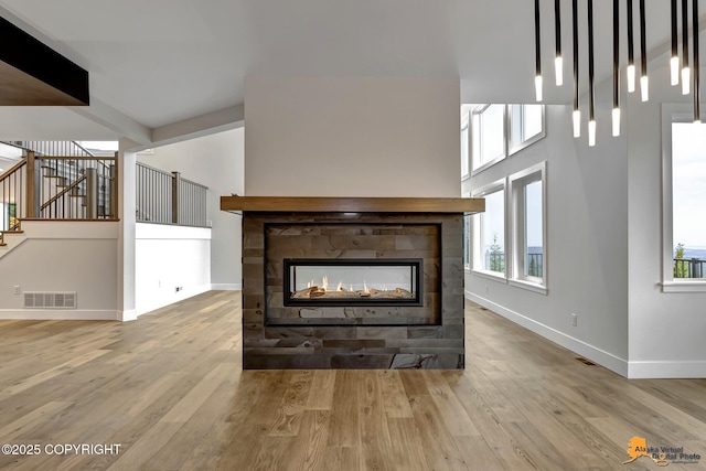 living room with a multi sided fireplace, visible vents, baseboards, and wood finished floors