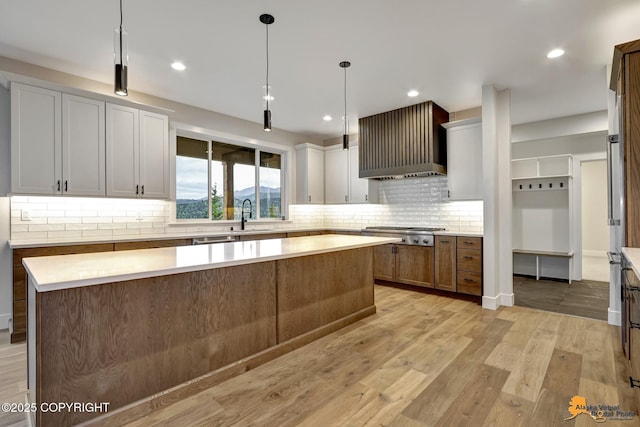 kitchen with light countertops, wall chimney range hood, light wood finished floors, and a center island