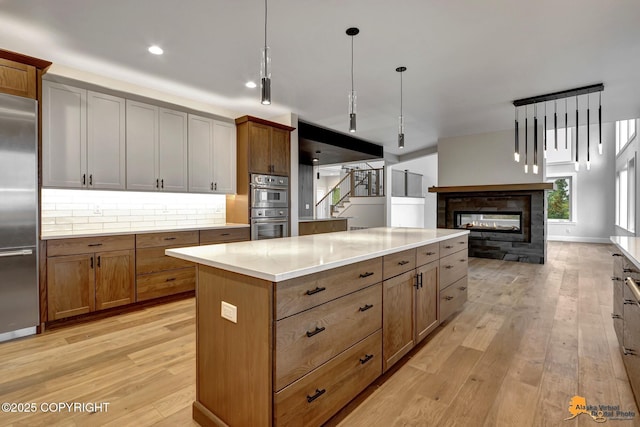 kitchen featuring stainless steel appliances, a multi sided fireplace, a kitchen island, and light wood-style flooring