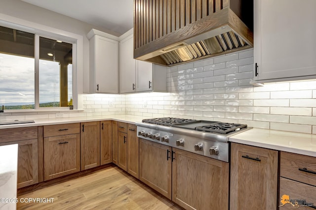 kitchen featuring stainless steel gas cooktop, light countertops, custom range hood, light wood-style floors, and tasteful backsplash