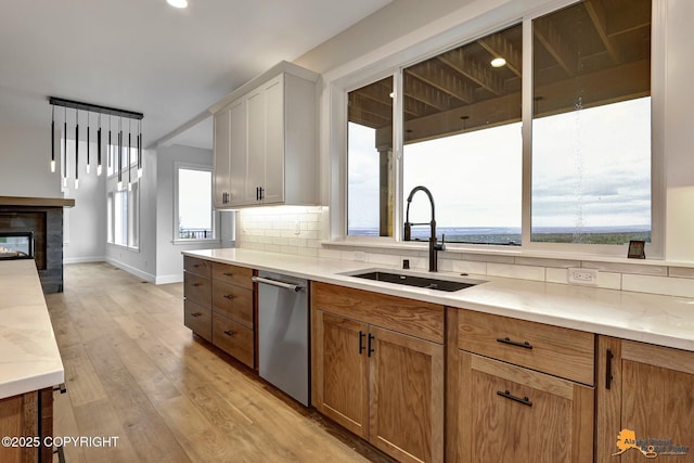 kitchen featuring light wood-style flooring, a sink, tasteful backsplash, stainless steel dishwasher, and a multi sided fireplace