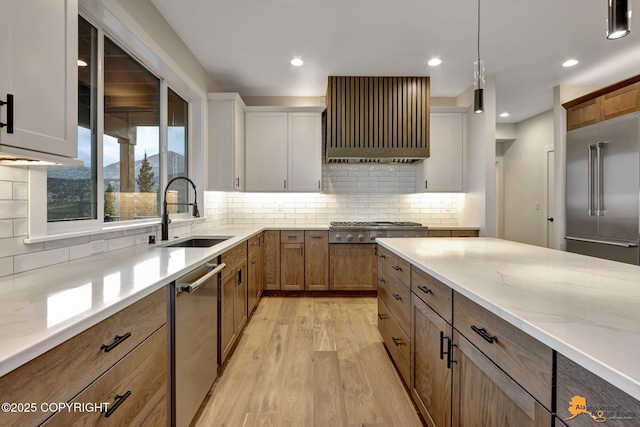 kitchen featuring light stone countertops, a sink, appliances with stainless steel finishes, light wood-type flooring, and backsplash