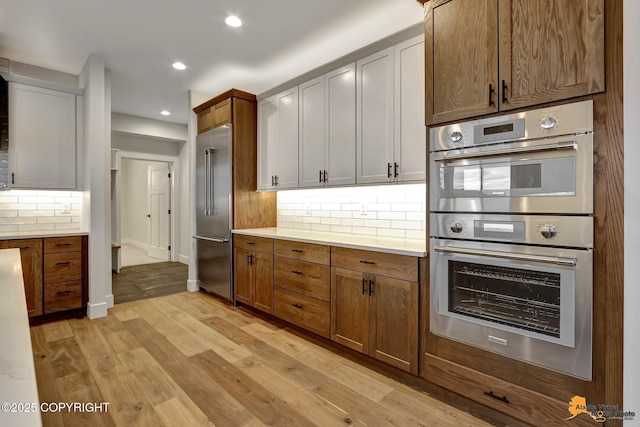 kitchen featuring recessed lighting, light countertops, light wood-style floors, appliances with stainless steel finishes, and backsplash