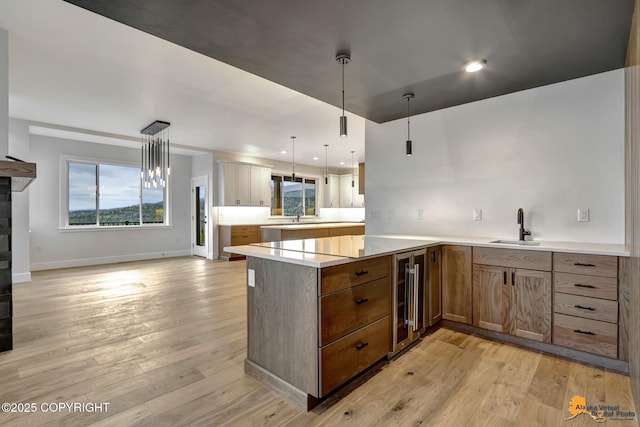 kitchen with wine cooler, a peninsula, light wood-type flooring, and a sink