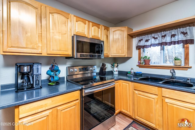 kitchen with dark countertops, light brown cabinetry, light wood-type flooring, stainless steel appliances, and a sink