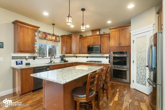 kitchen featuring a sink, a kitchen island, appliances with stainless steel finishes, decorative backsplash, and dark wood-style flooring