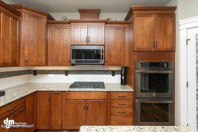 kitchen featuring light stone counters, brown cabinets, backsplash, and appliances with stainless steel finishes