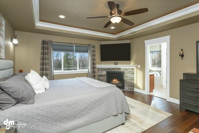 bedroom featuring hardwood / wood-style floors, a raised ceiling, baseboards, and a tiled fireplace