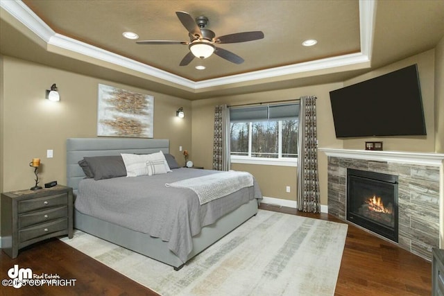 bedroom with a tray ceiling, wood finished floors, a tiled fireplace, and ornamental molding