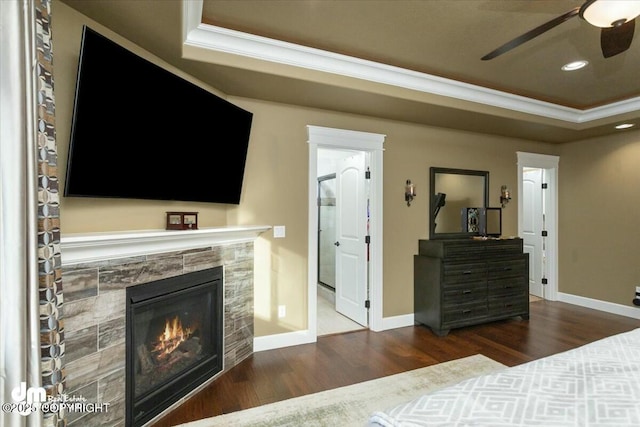 bedroom featuring ornamental molding, a tiled fireplace, a tray ceiling, wood finished floors, and baseboards