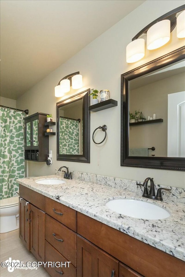 full bathroom featuring double vanity, curtained shower, toilet, and a sink