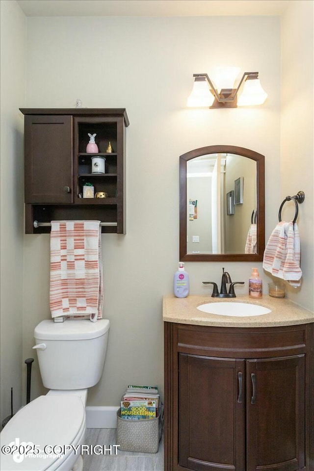 bathroom featuring baseboards, toilet, wood finished floors, and vanity