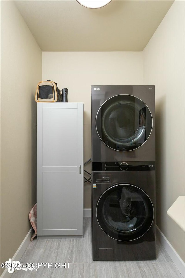 clothes washing area featuring wood finished floors, baseboards, and stacked washer / drying machine