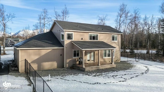 snow covered property with french doors, roof with shingles, a deck, and fence