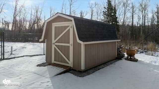 snow covered structure with a storage shed, fence, and an outdoor structure