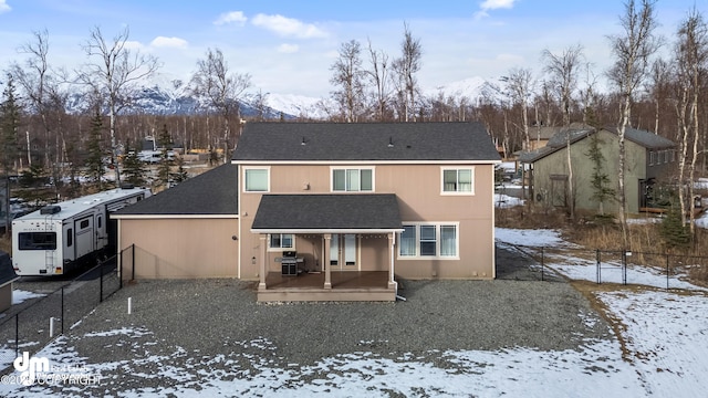 snow covered rear of property with a shingled roof and fence