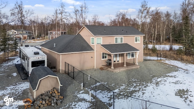 snow covered rear of property with a fenced backyard, roof with shingles, and a wooden deck