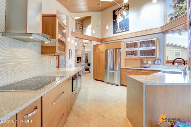 kitchen with a sink, freestanding refrigerator, black electric cooktop, light stone countertops, and extractor fan