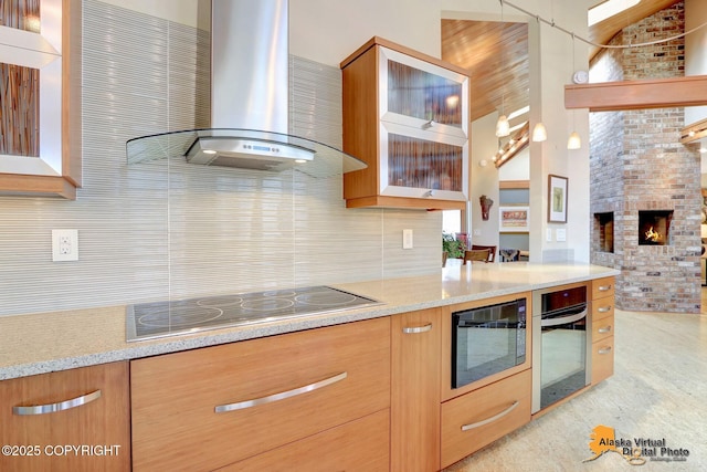 kitchen featuring light stone counters, wall chimney range hood, stainless steel oven, decorative backsplash, and black electric stovetop