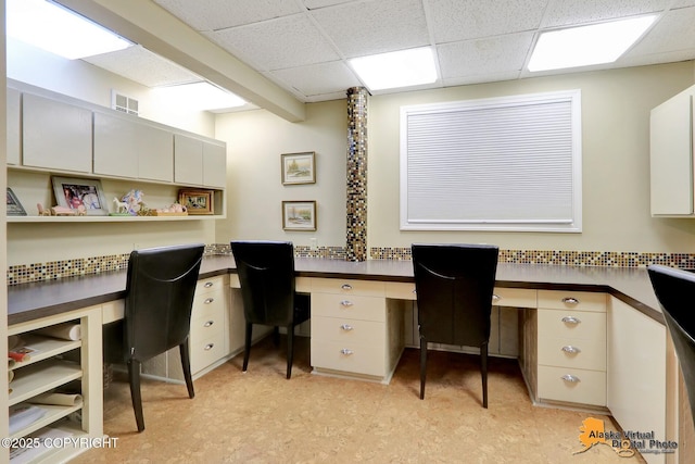 home office featuring a drop ceiling, visible vents, light floors, and built in desk