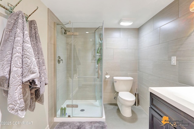 bathroom with toilet, a stall shower, vanity, and tile walls