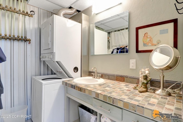 full bathroom with vanity, a textured wall, and stacked washer and dryer