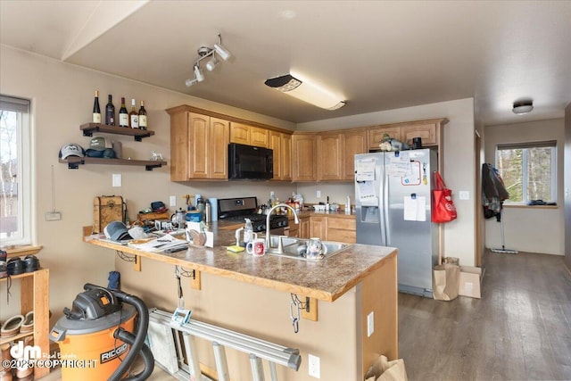 kitchen with a healthy amount of sunlight, wood finished floors, a peninsula, a sink, and appliances with stainless steel finishes