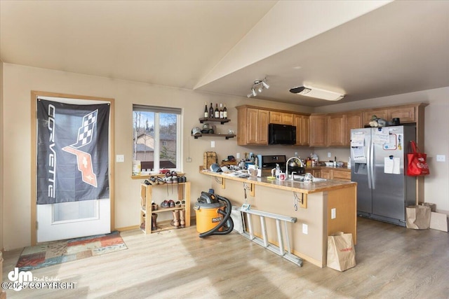 kitchen with light wood finished floors, a breakfast bar, a peninsula, a sink, and appliances with stainless steel finishes