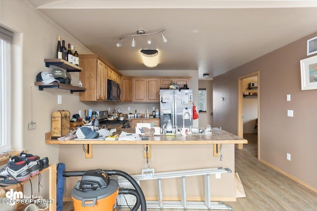 kitchen featuring black microwave, a peninsula, light wood-style floors, stainless steel refrigerator with ice dispenser, and stove