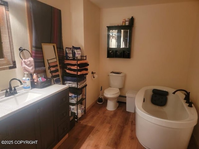 full bath featuring vanity, wood finished floors, a freestanding tub, toilet, and baseboard heating