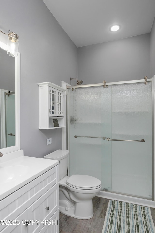 bathroom featuring wood finished floors, toilet, a stall shower, and vanity