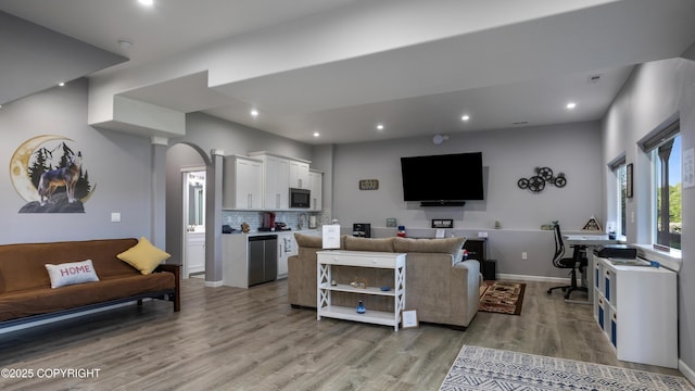 living room featuring recessed lighting, baseboards, arched walkways, and light wood finished floors