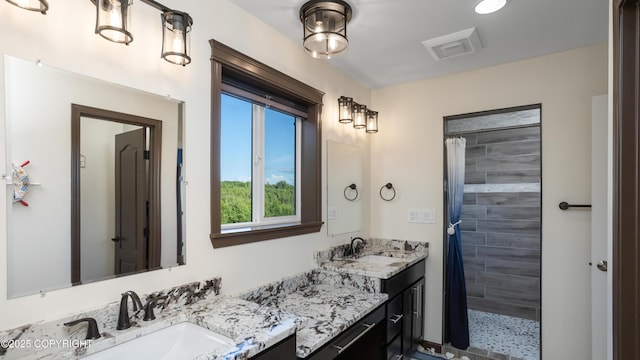 bathroom with visible vents, tiled shower, and vanity