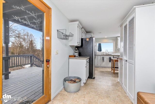 kitchen with a sink, white cabinets, freestanding refrigerator, and light countertops