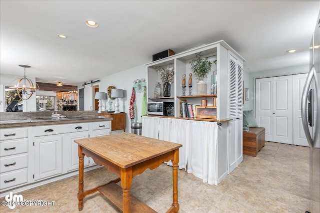 kitchen with a sink, white cabinetry, a barn door, appliances with stainless steel finishes, and a chandelier