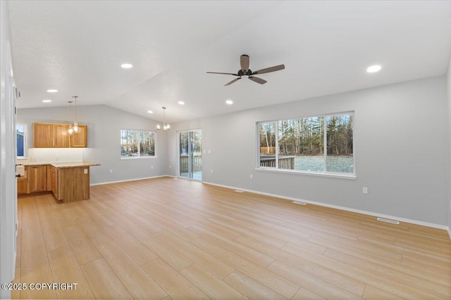 unfurnished living room with lofted ceiling, light wood-style flooring, plenty of natural light, and ceiling fan with notable chandelier